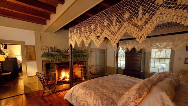 A cozy bedroom with a fireplace, a four-poster bed, and a lace canopy.