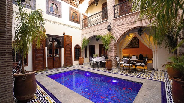 Un patio con piscina, plantas en macetas y mobiliario exterior.