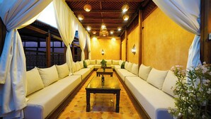 Una habitación con un sofá largo frente a una mesa, cortinas en las ventanas y luces fijadas a la pared.