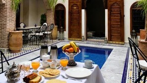 Comedor con piscina, con una mesa dispuesta para el desayuno, rodeado de arquitectura tradicional marroquí.
