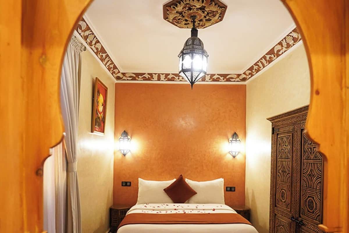 Una habitación acogedora con cama, una mesita, una lámpara decorativa y un tapete estampado.