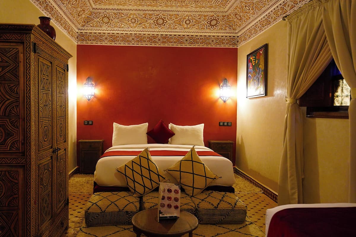 Habitación de hotel con una cama grande, dos lámparas de pared, un techo decorativo y una ventana con cortinas.