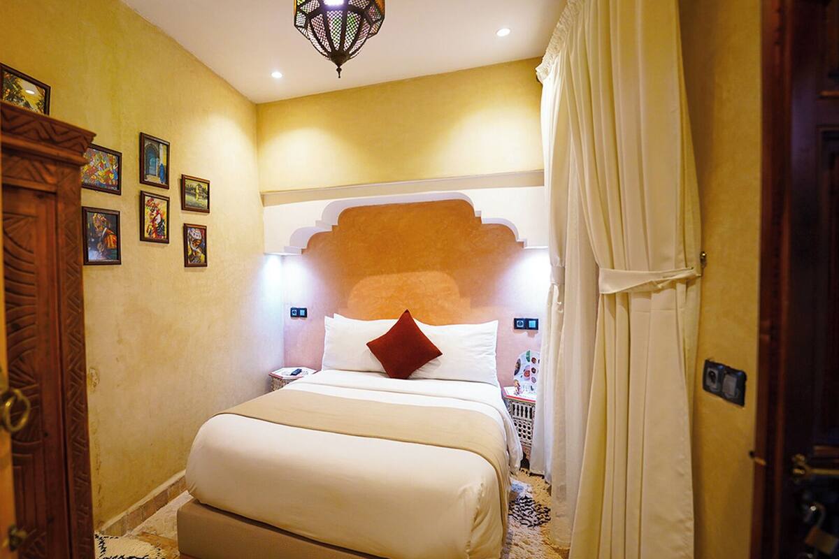 Una habitación de hotel con una cama grande, un armario de madera y una lámpara decorativa en el techo.