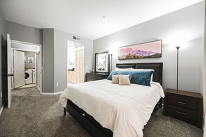 Une chambre à coucher comprenant un lit, des tables de chevet, une commode, une coiffeuse et un téléviseur fixé au mur.