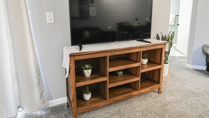 A flat-screen TV mounted on a wooden TV stand with three shelves, each holding a potted plant.