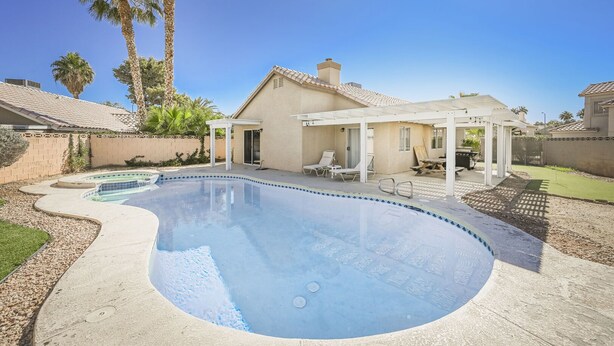 A swimming pool with a curved design, surrounded by a patio area with lounge chairs and a pergola. - SVS: 3BD/2BA Residential Home | Quiet Neighborhood | Sleeps 6 (Las Vegas)