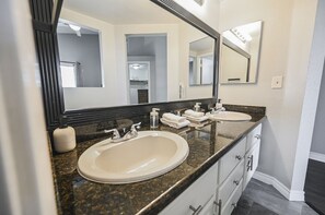 Une salle de bain avec deux lavabos, un grand miroir et un comptoir en granit.