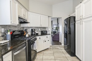 Une cuisine moderne avec des meubles blancs, une cuisinière noire et un réfrigérateur noir.
