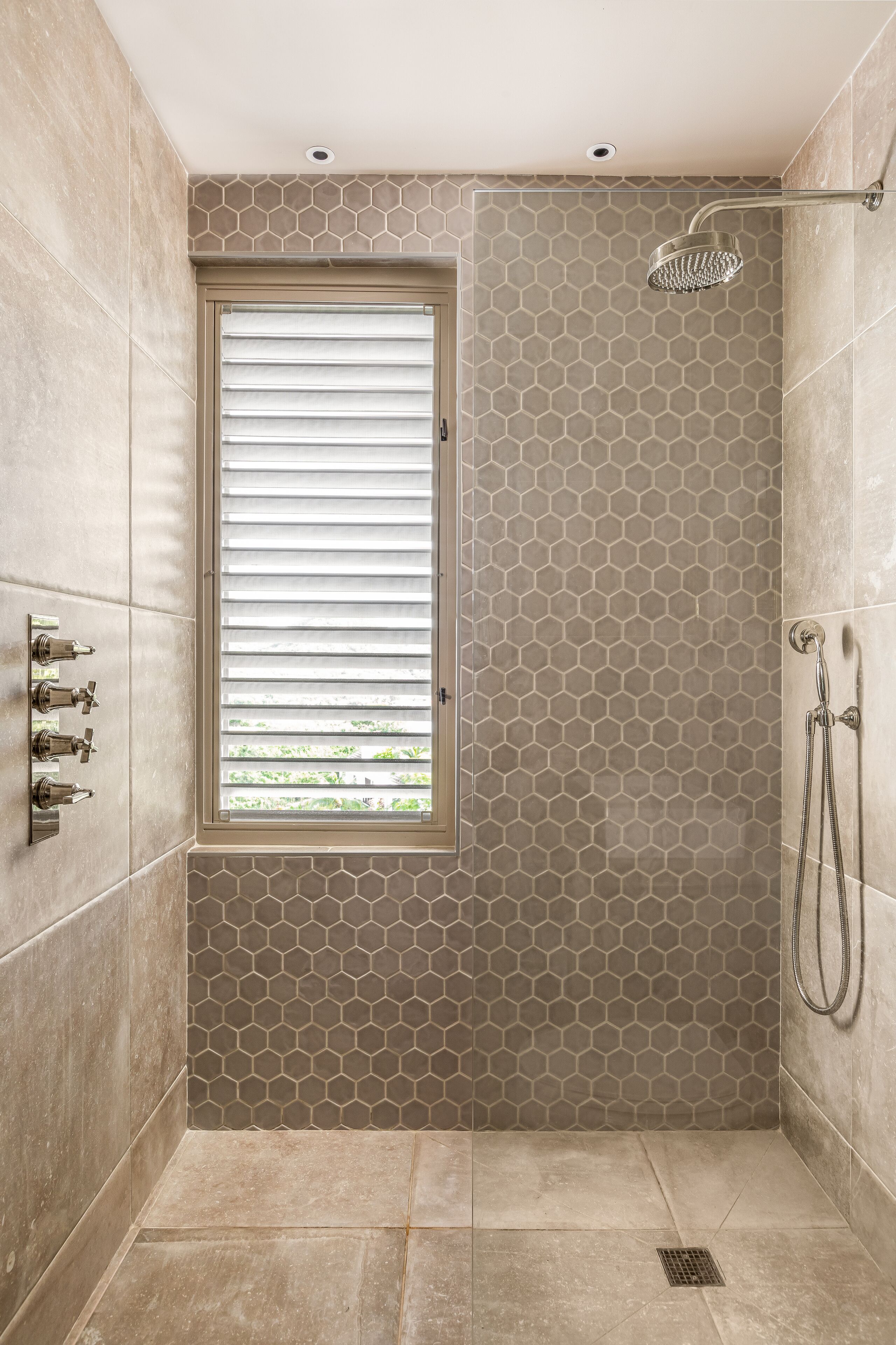 A walk-in shower with a window, hexagonal tile pattern, and a showerhead.