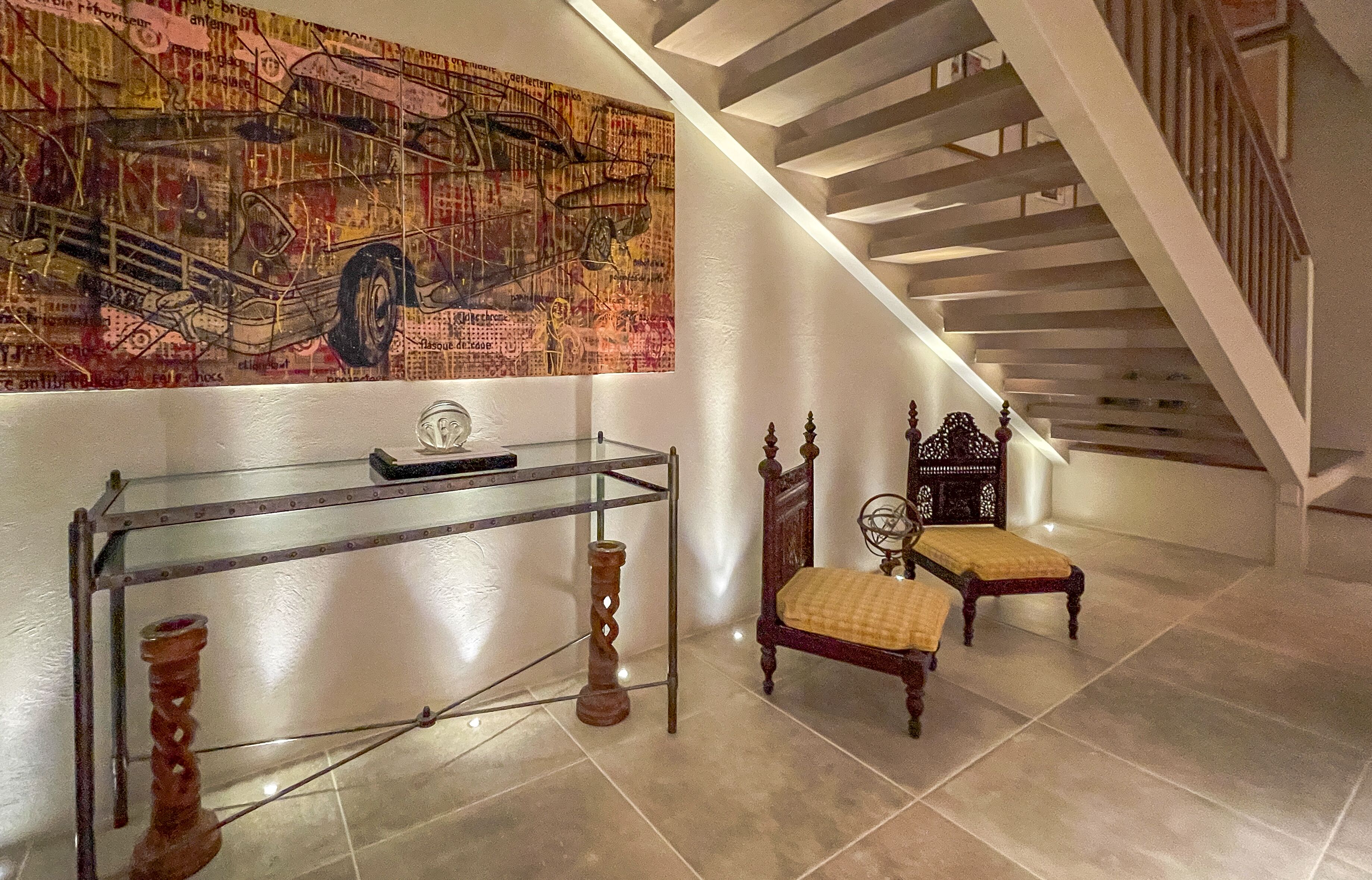 A staircase with a glass railing, a wooden bench with a cushion, and a wall with a large abstract painting.