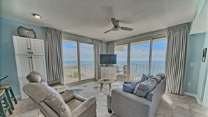 A spacious living room with a sofa, armchair, and a television on a stand. There is a balcony with a view of the ocean. - Shores of Panama 503~End Unit 3 Bdrm (Panama City Beach)