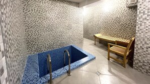 Une salle de bain avec un mur carrelé, une baignoire recouverte de carreaux bleus, un banc en bois et un espace douche.