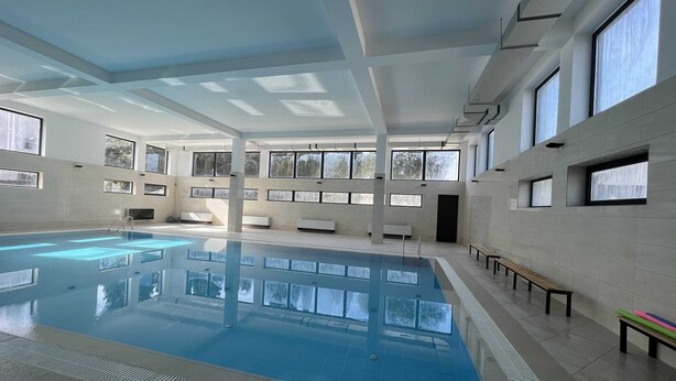 Une piscine intérieure à l’eau claire, entourée de murs recouverts de carreaux et dotée de grandes fenêtres.