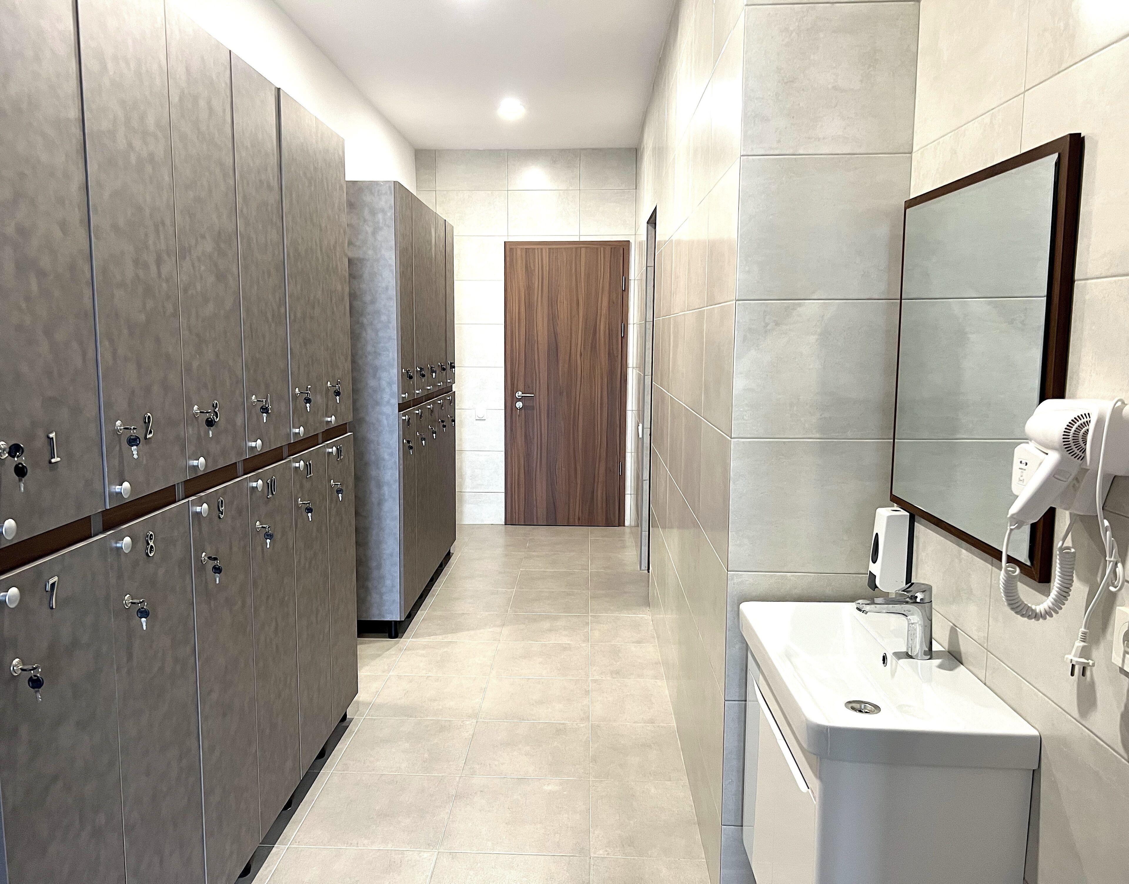 Un baño moderno con taquillas, una puerta de madera, un lavamanos y un secador de pelo.
