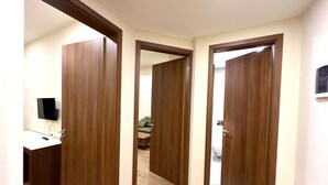 Un couloir avec des portes en bois menant  à une pièce où se trouvent un canapé et un téléviseur.