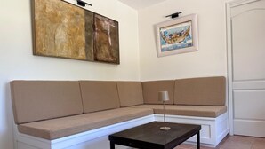 Quarto de canto com um sofá seccional bege, uma pequena mesa preta e duas obras de arte nas paredes.