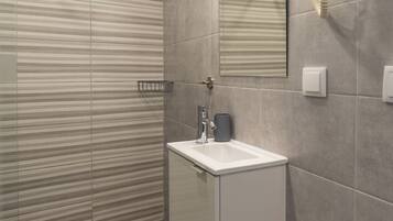 Baño con ducha, lavamanos, espejo y secador de pelo montado en la pared.