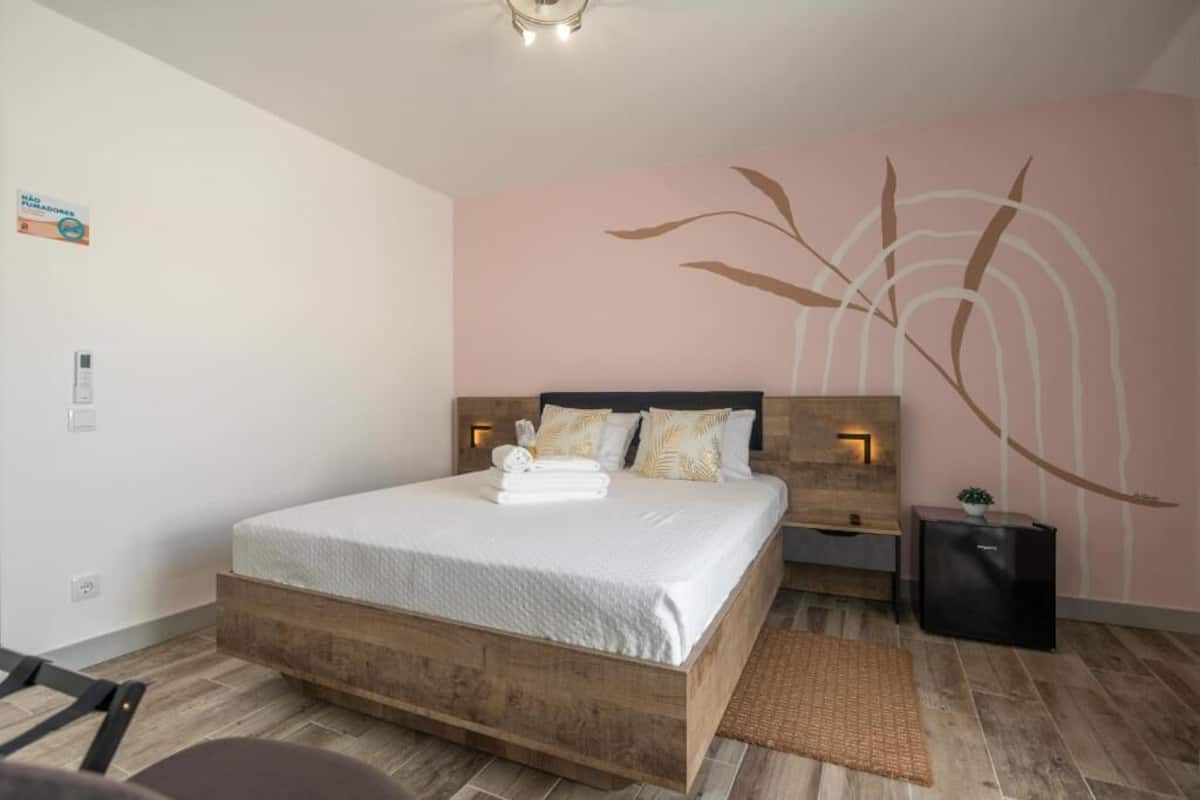 A bedroom with a wooden bed, a nightstand, a wall-mounted lamp, and a small plant.