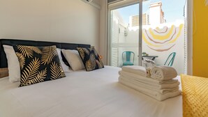 Habitación de hotel con una cama, almohadas, una pila de toallas y una vista a través de un ventanal.