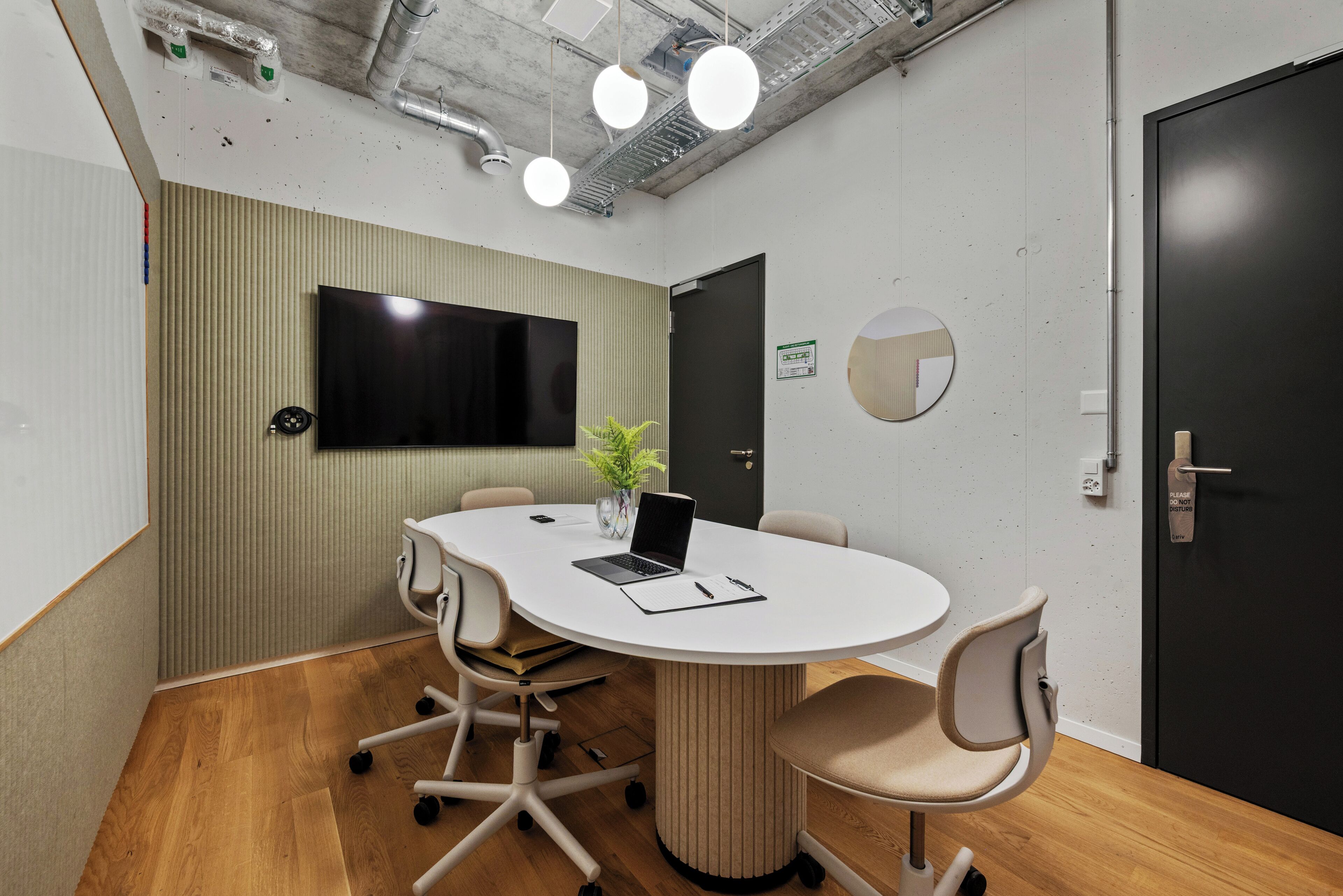 Une salle de conférence avec une table ronde, quatre chaises, un ordinateur portable, une plante et un téléviseur fixé au mur.