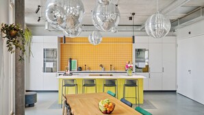 Una cocina moderna con detalles amarillos, un comedor con mesa y sillas de madera, y bolas de discoteca colgantes.