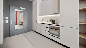Una cocina moderna con armarios blancos, horno integrado y encimera con fregadero y cafetera.