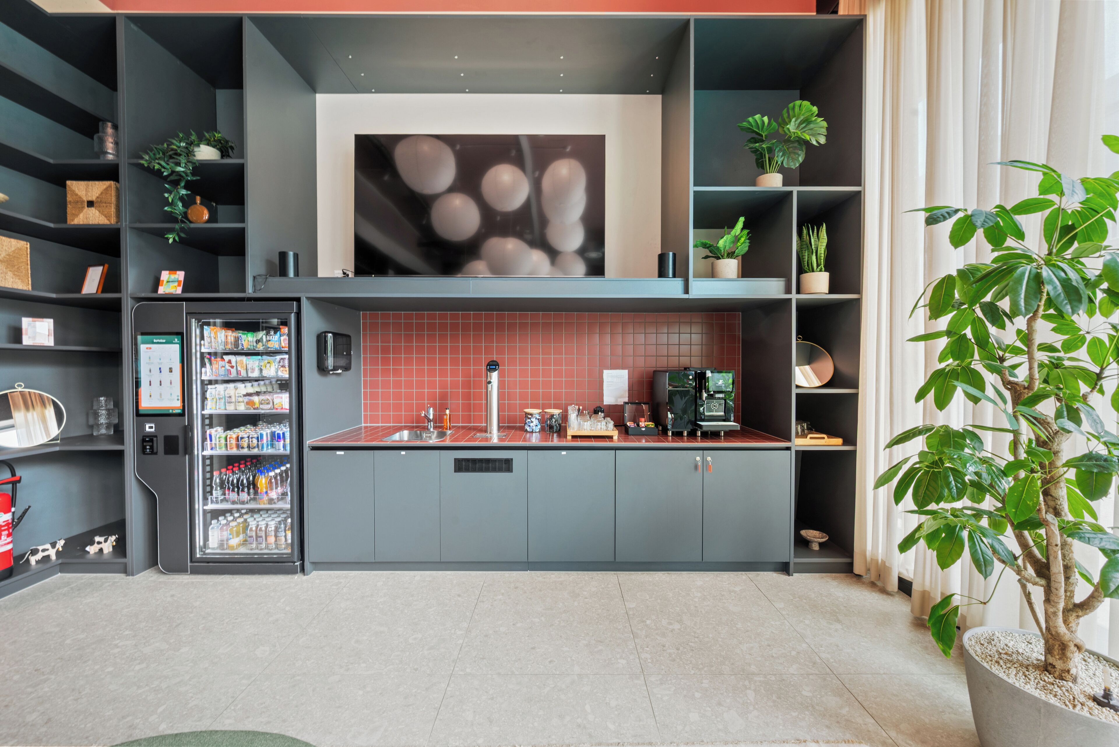 A modern kitchen with grey cabinets, a red backsplash, and a built-in coffee machine.