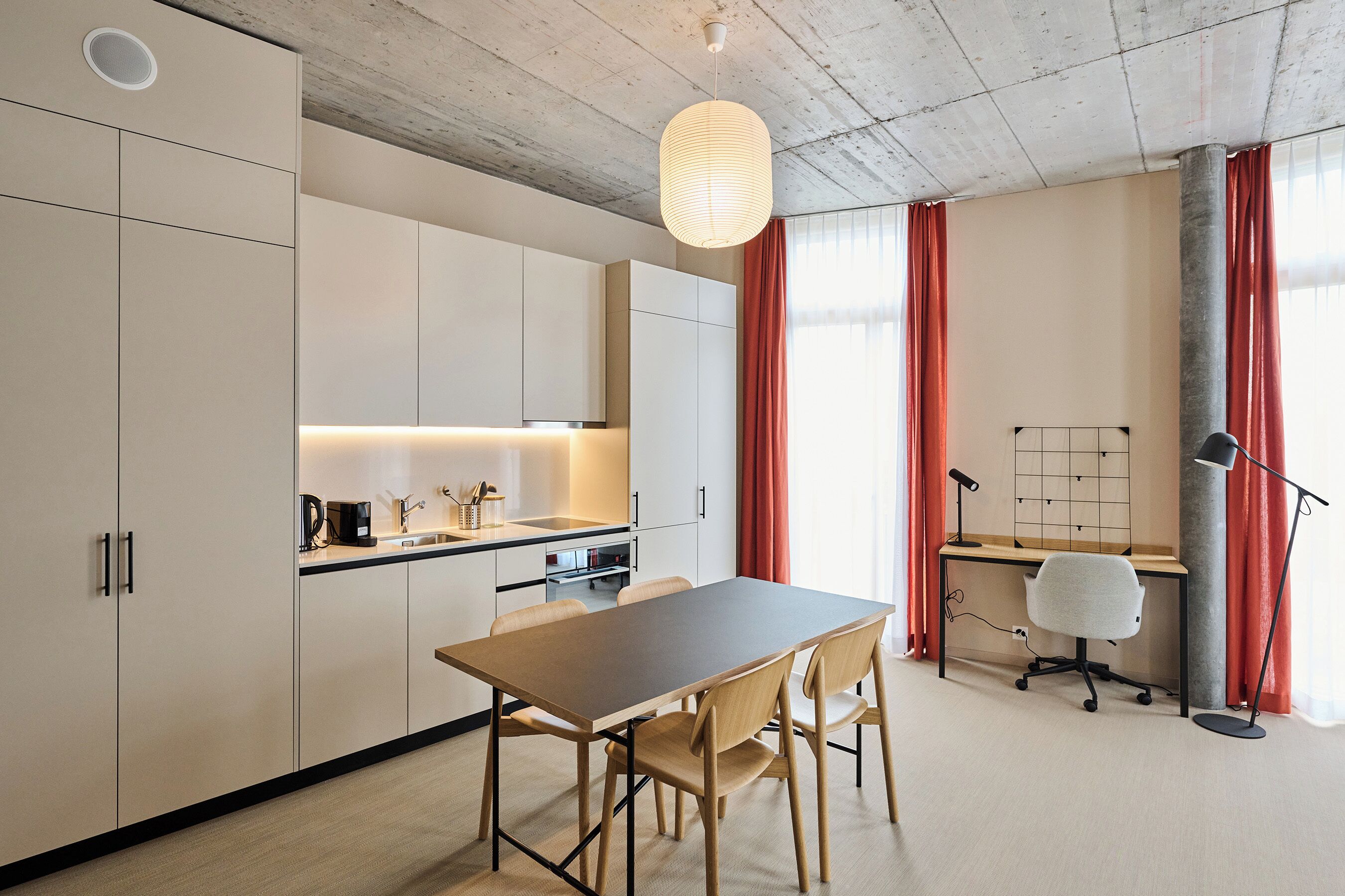 A modern kitchen with white cabinets, a wooden dining table, and a pendant light.