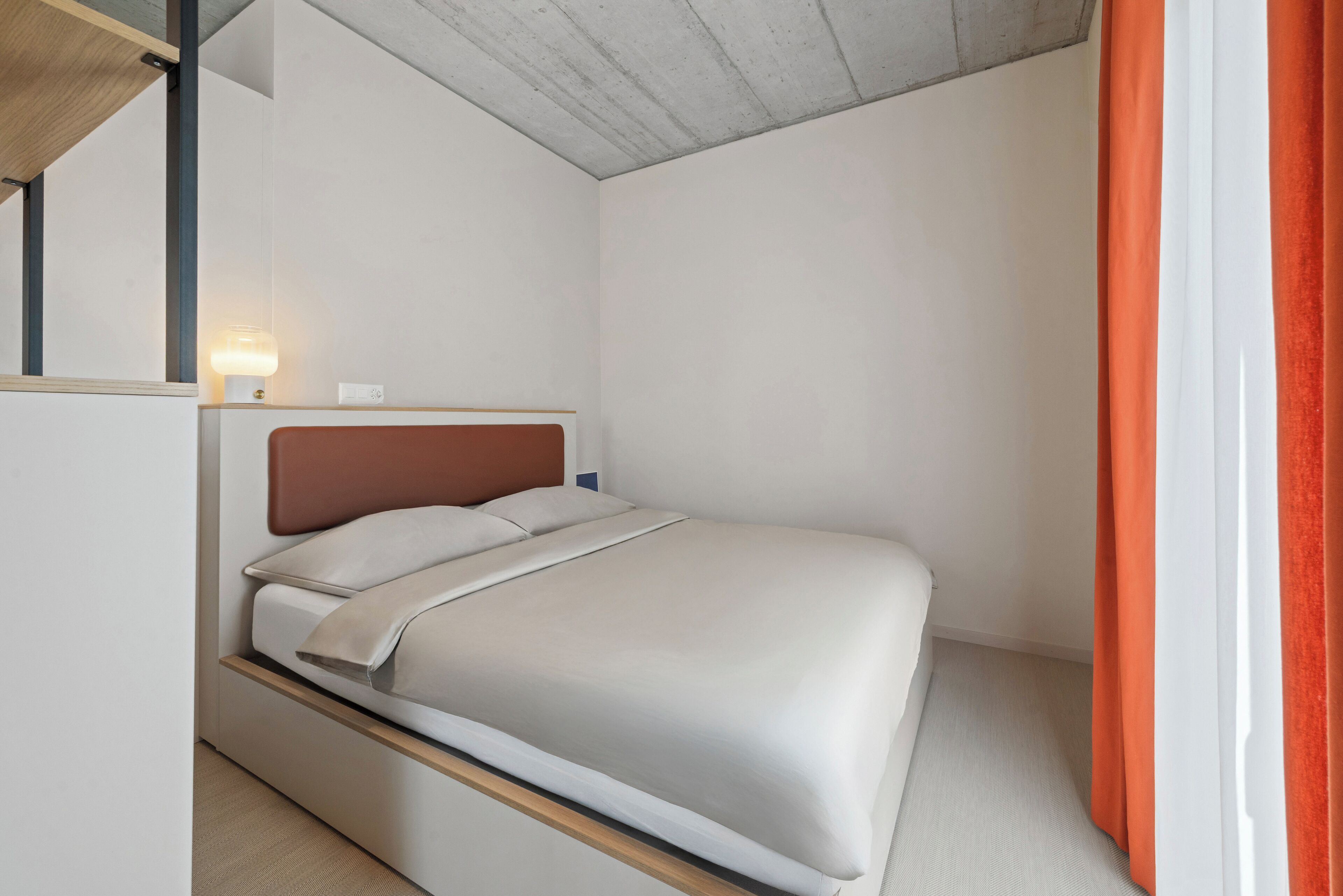 A minimalist bedroom with a bed, a nightstand, and a wall-mounted lamp.