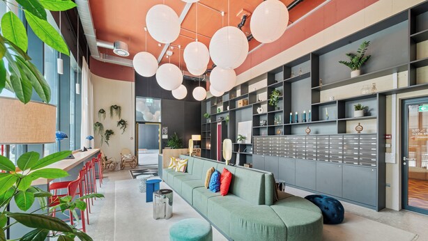 Un interior moderno con un sofá verde curvo, sillas rojas y una planta grande.