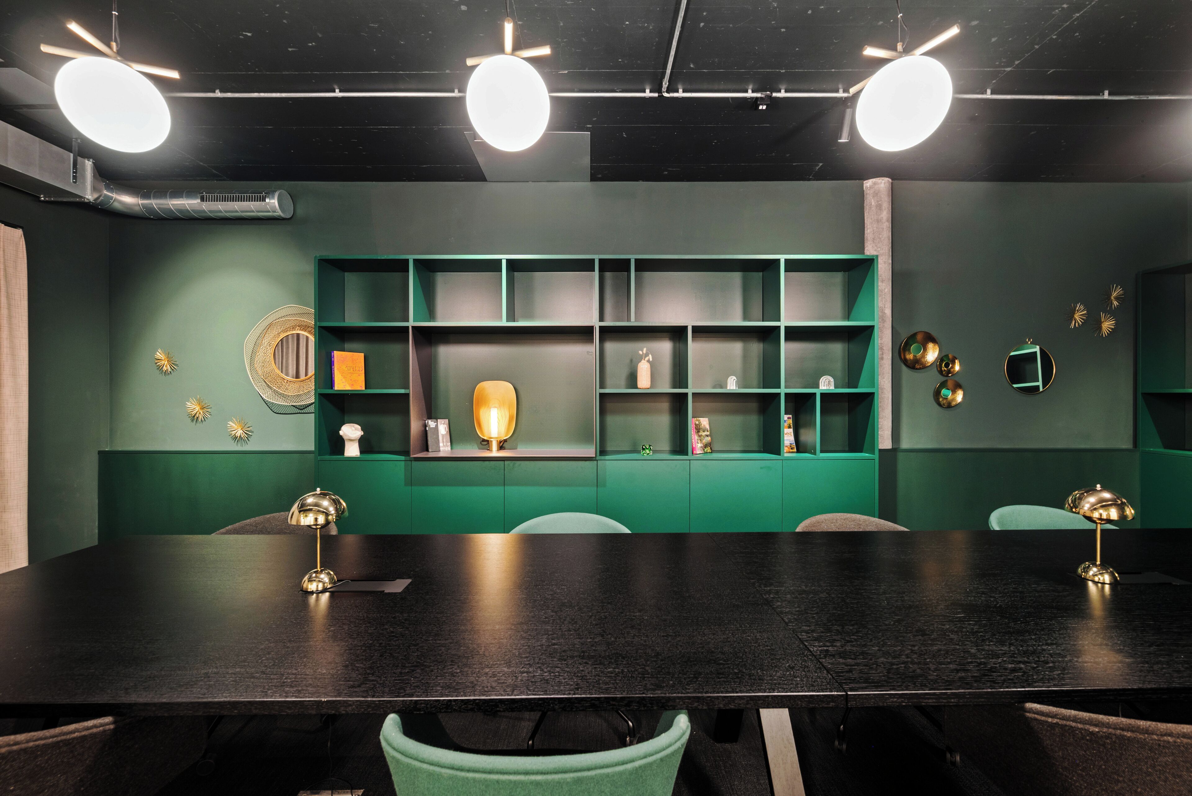 Un salón de conferencias con una mesa oscura, estanterías verdes y luminarias modernas.