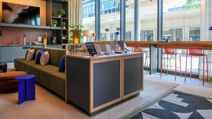 Un moderno vestíbulo de hotel con un mostrador de recepción, zona de estar y grandes ventanales que ofrecen vistas del exterior del edificio.