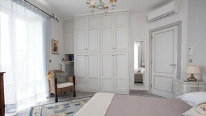 Ein Schlafzimmer mit einem großen Bett, einem Kleiderschrank, einem Sessel, einem Nachttisch und einem Spiegel.