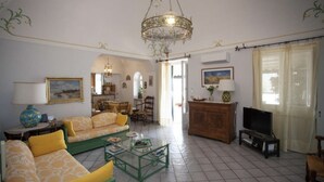 Ein Wohnzimmer mit einer Sofagarnitur, einem Fernseher, einer Kristallleuchtre und einem Essbereich.