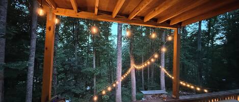 A wooden deck with string lights, a table, and a bench.