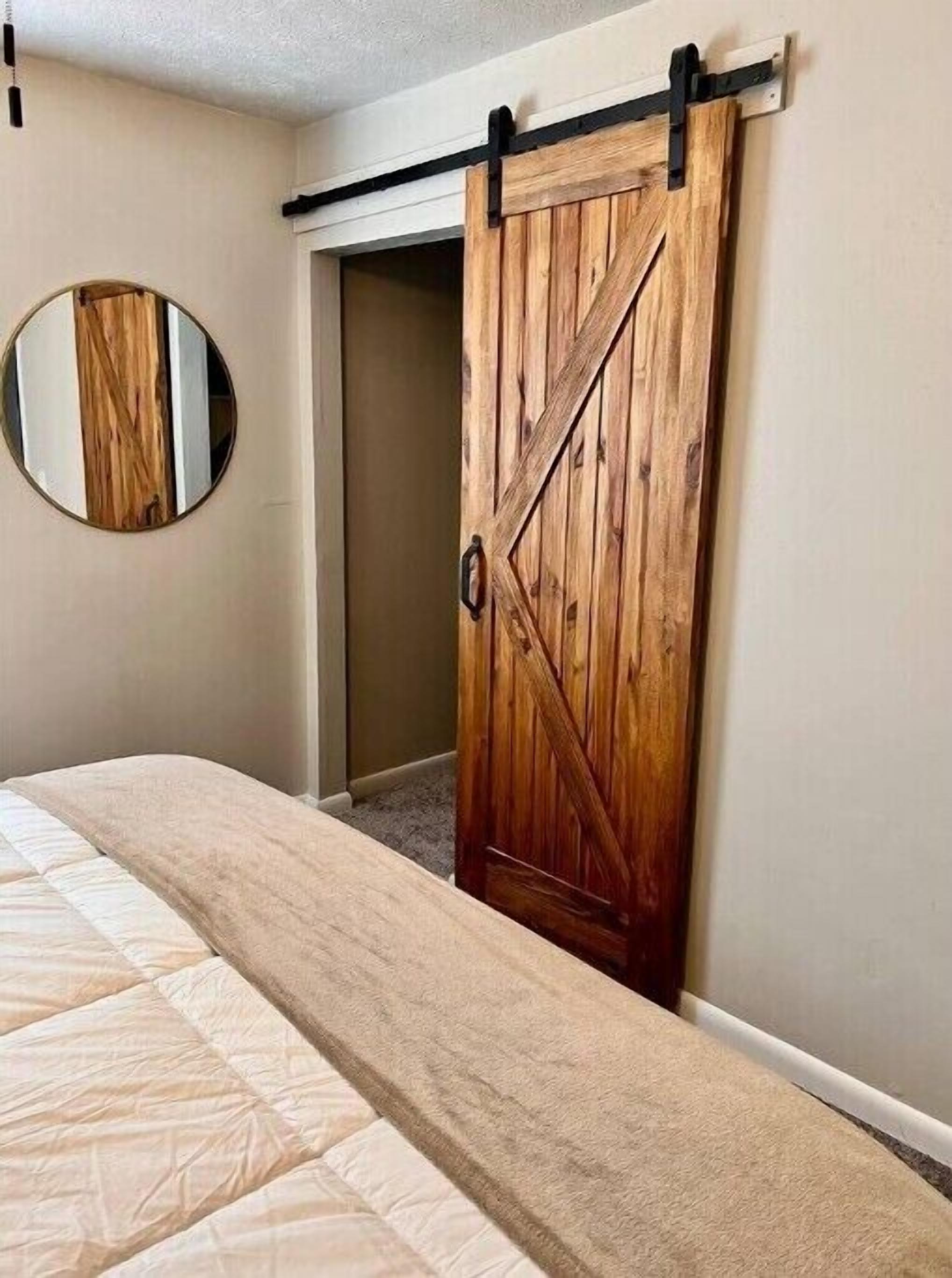 A bedroom with a large bed, a wooden sliding door closet, and a round mirror on the wall.