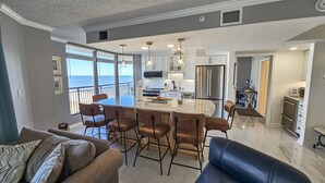 A spacious living area with a large island, bar stools, and a view of the ocean.