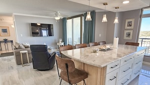 A modern kitchen with a marble island, bar stools, and pendant lighting.
