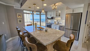 A kitchen with a large island, bar stools, stainless steel appliances, and a view of the ocean.
