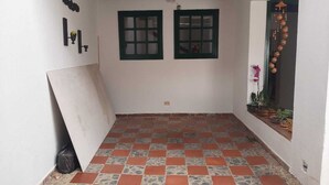 Una habitación con piso a cuadros, dos ventanas con marcos verdes, una viga de techo negra y una lámpara fijada a la pared.