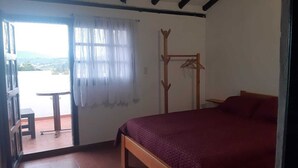 Un dormitorio con cama, un banco de madera, una ventana con cortinas translúcidas y vistas al exterior.