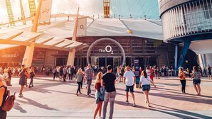 A modern building with a prominent circular logo and a large open plaza with people walking.