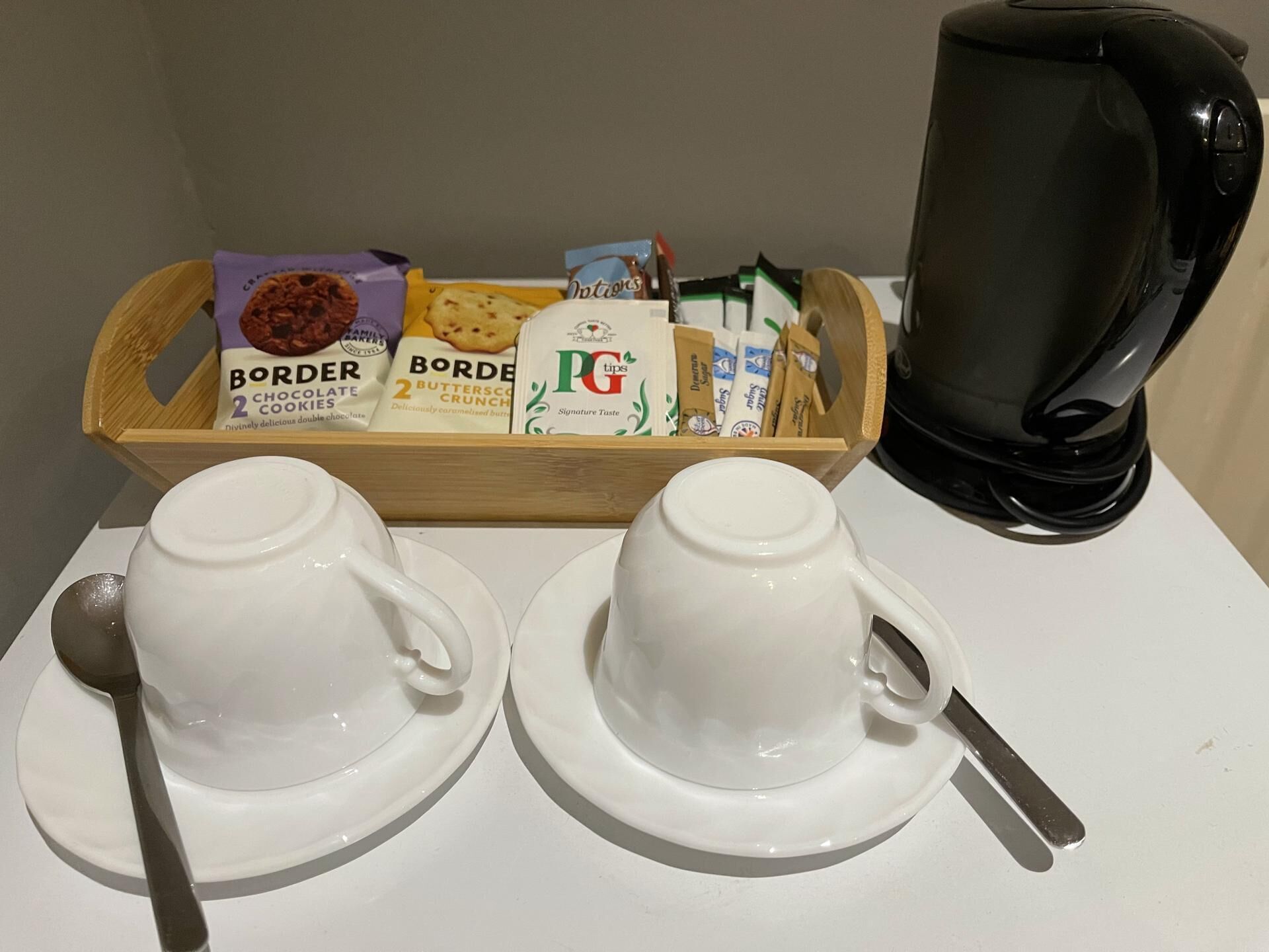 A breakfast tray with two cups of coffee, a spoon, and assorted snacks including chocolate and biscuits.