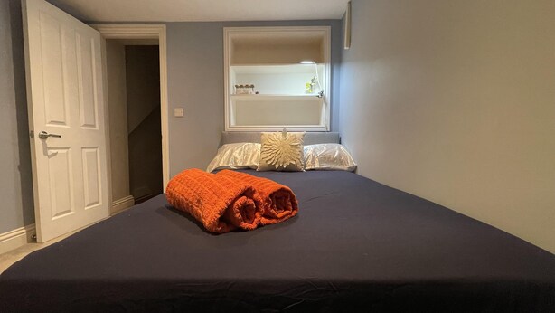 A bedroom with a bed, a window with a view, a door, and a small shelf with items.