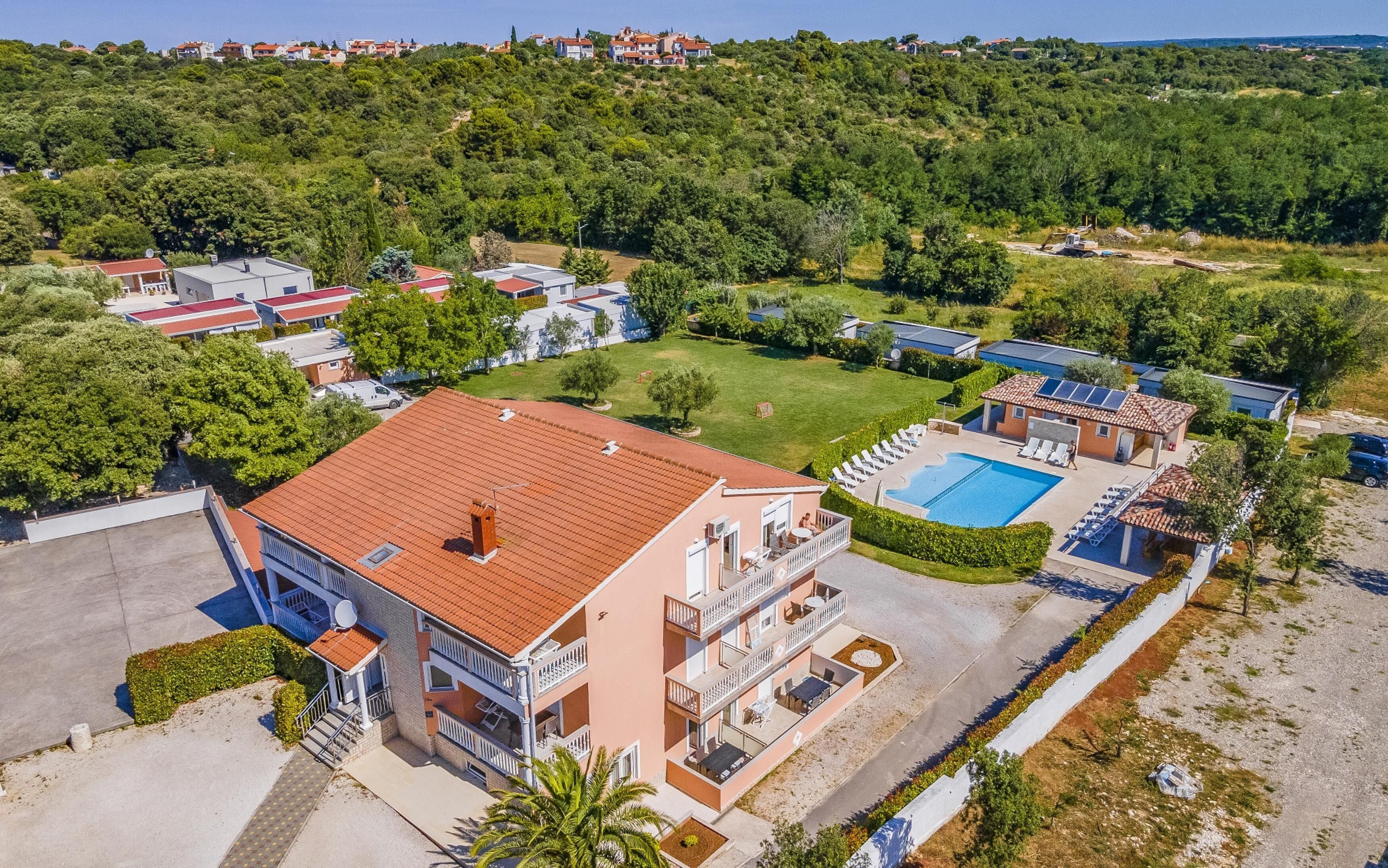 An aerial view of a residential area with a large building featuring multiple balconies, a swimming pool, and a well-maintained lawn.