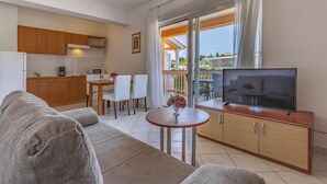 A modern living room with a sofa, a TV on a wooden cabinet, a dining table with chairs, and a balcony with a view. - Apartments with Shared Pool Rocco 1 (Medulin)