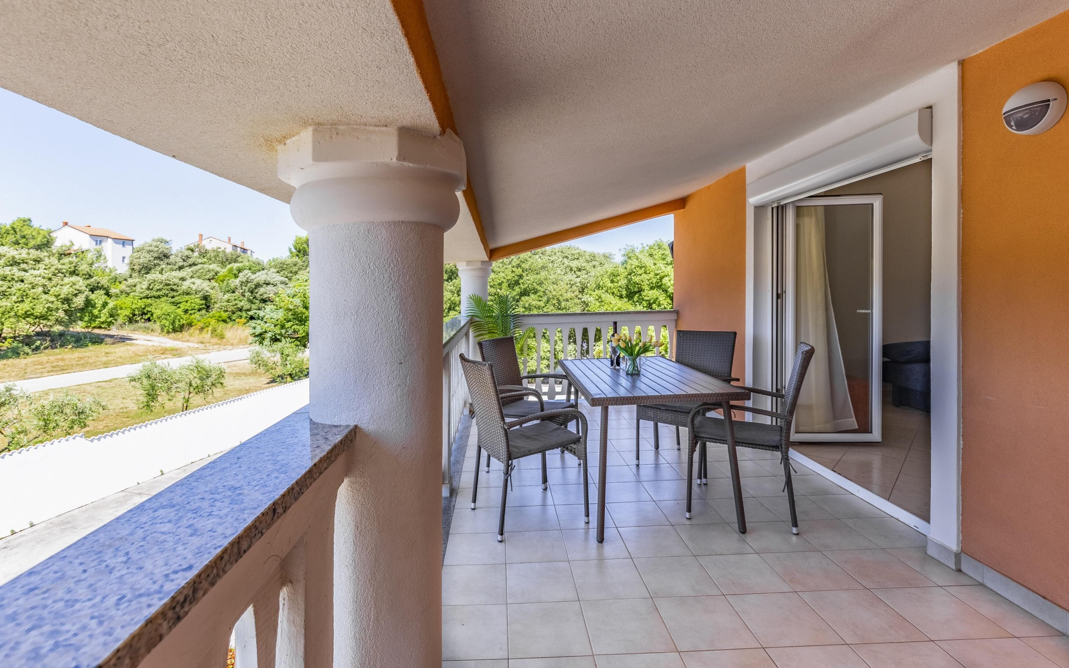 Un balcon avec une table et des chaises, une vue sur la verdure et un bâtiment en arrière-plan.