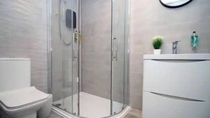 Ett modernt badrum med en duschavdelning med glasväggar, en vit toalett och en tvättställsmöbel med spegel och hygienartiklar.