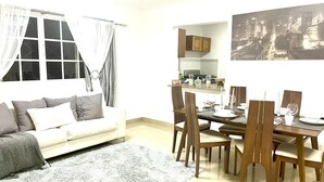 Una sala de estar con sofá, una mesa de comedor con sillas, una zona de cocina y un cuadro de un paisaje urbano en la pared.