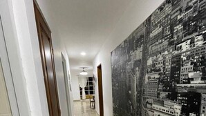 Un pasillo con un gran mural de un paisaje urbano en la pared derecha, una puerta a la izquierda y un ventilador de techo en el centro.